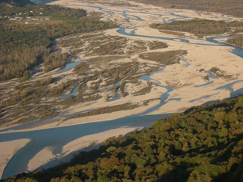 Braided river channels of the Tagliamento at Cornino, Italy, with multiple shallow threads weaving around exposed gravel bars under alpine cliffs