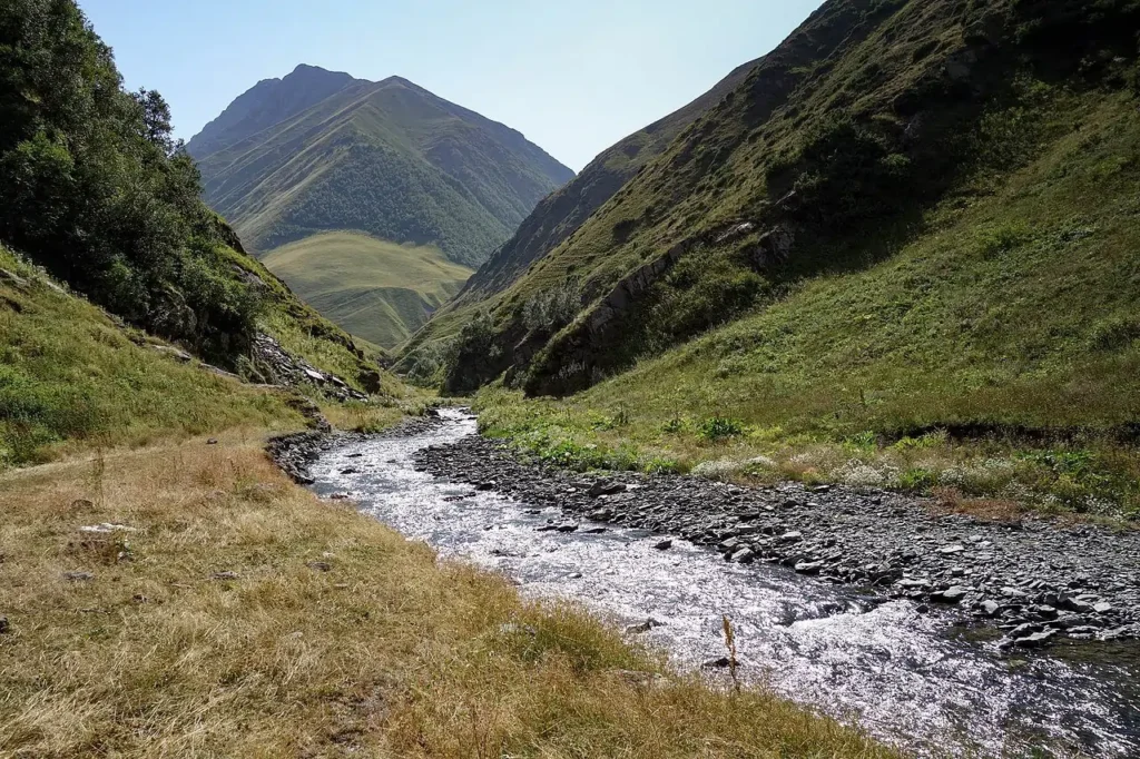 Steep V-shaped river valley cut into bedrock by a young stream in Georgia, showing the dominance of vertical erosion over lateral erosion in upper river reaches