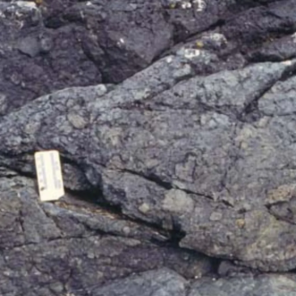 Primer plano de rocas grises estratificadas con una pequeña escala (aglomerado)
