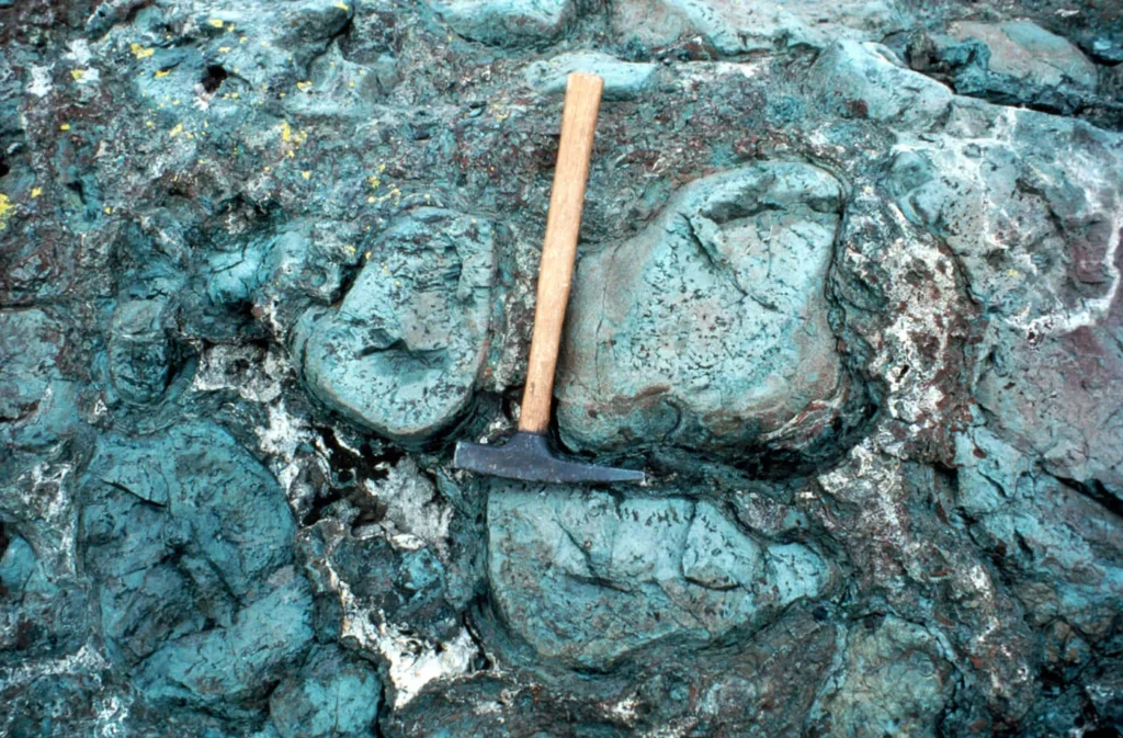 Martillo de geólogo sobre lavas almohadilladas verdosas (hialoclastita)