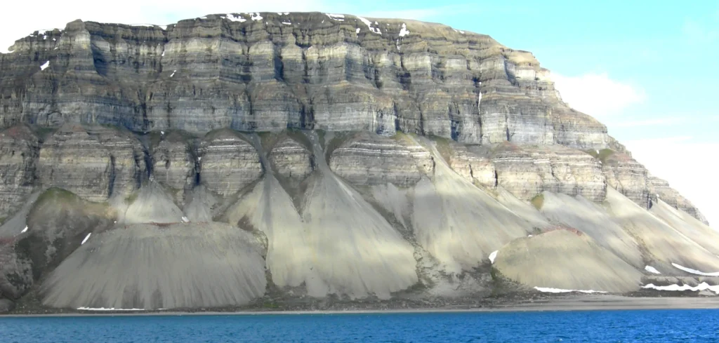 Montaña de laderas escarpadas y estratificadas sobre aguas árticas azules (movimientos de ladera)