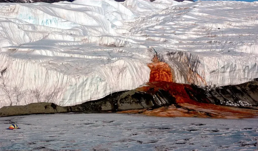 Blood Falls, the rust-red waterfall flowing from the snout of Taylor Glacier onto the ice of West Lake Bonney in Antarctica, with a field tent at left for scale