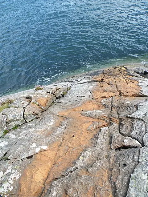 Closely spaced finely laminated rock layers with visible soft-sediment deformation, photographed on a Garvellach Islands shore