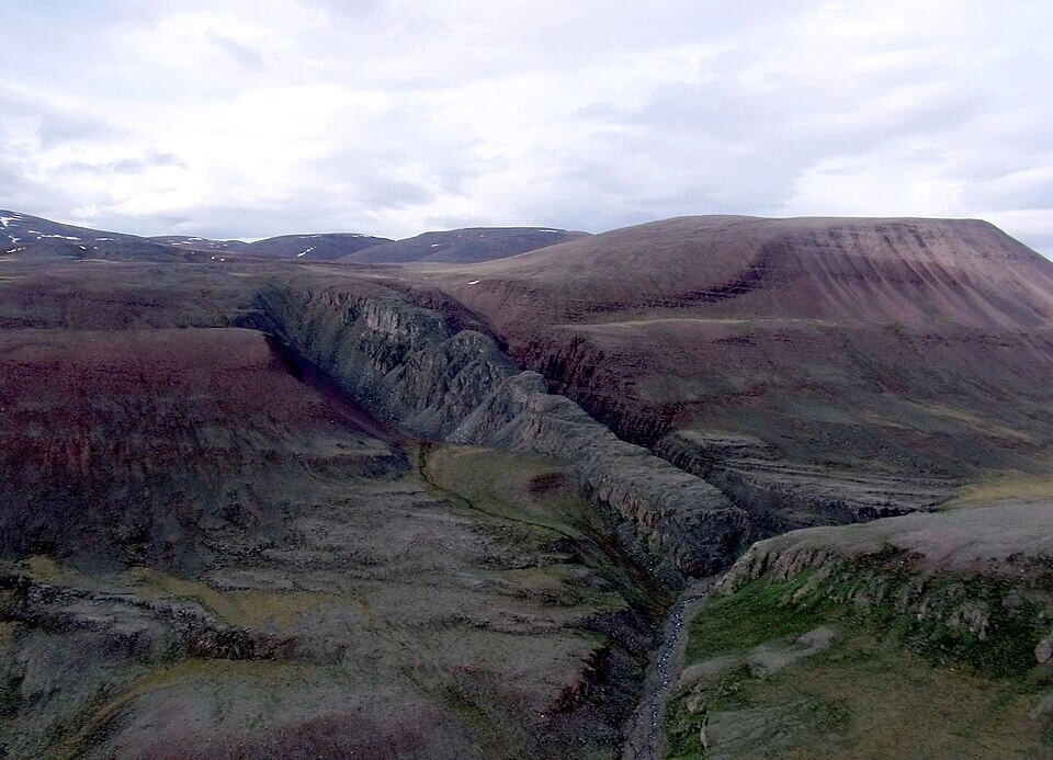 A dark vertical basaltic dike cutting through pale country rock on a rocky Arctic coast