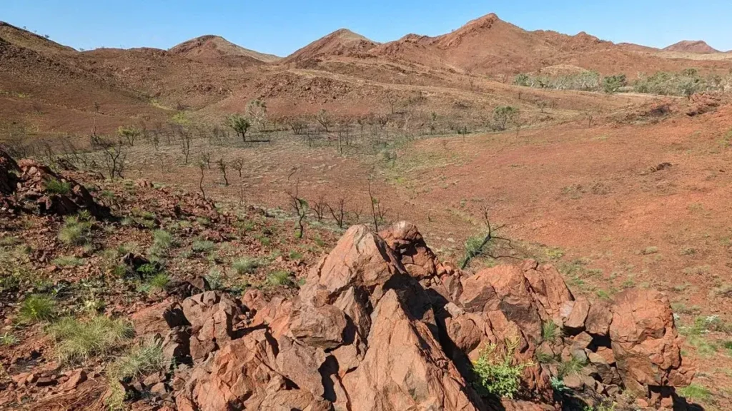 A meter-tall conical shatter cone in red Pilbara rock, with the rolling hills of the Antarctic Creek Member behind it