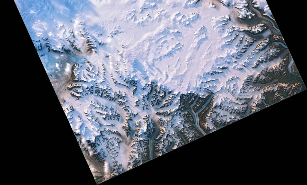 Natural-colour satellite view of glaciers and bare metamorphic mountains in eastern Greenland, with long shadows cast by low evening sun