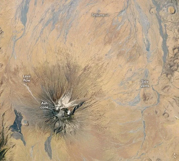 Astronaut photograph of Ol Doinyo Lengai stratovolcano in northern Tanzania, the symmetric "Mountain of God" of the Gregory Rift — the only active volcano on Earth currently erupting natrocarbonatite lava, with light-coloured lava flows and canyons radiating from its summit cone.