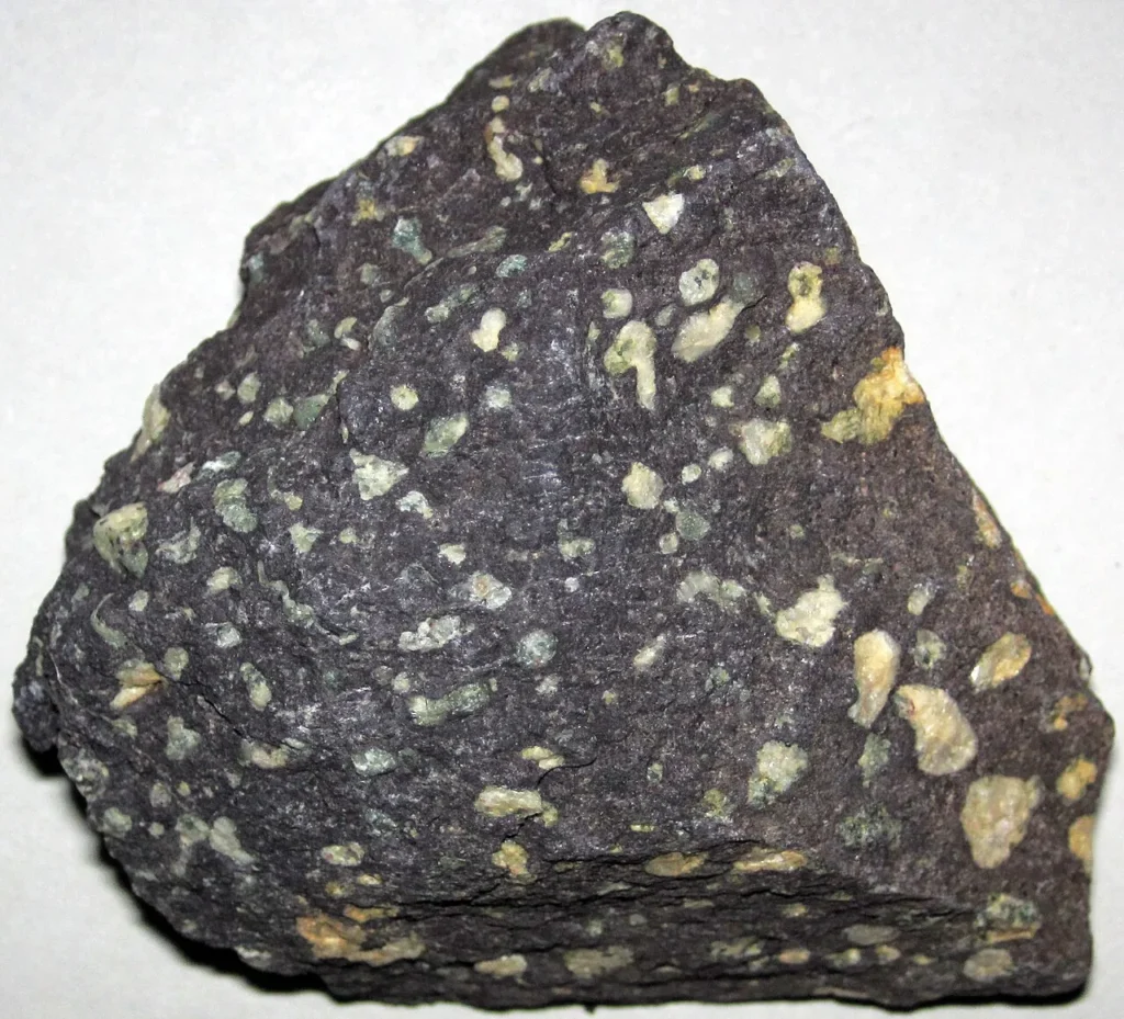 A hand sample of vesicular, amygdaloidal basalt showing numerous rounded gas-bubble cavities, some filled with pale minerals.