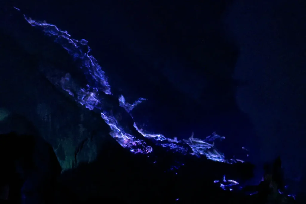 Blue flames and glowing molten sulfur flowing across rocks inside the Kawah Ijen crater