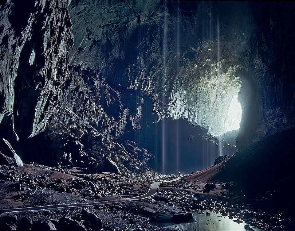The vast dark passage of Deer Cave in Gunung Mulu National Park, Borneo, its limestone walls receding into shadow, conveying the scale of the region's giant cave chambers.