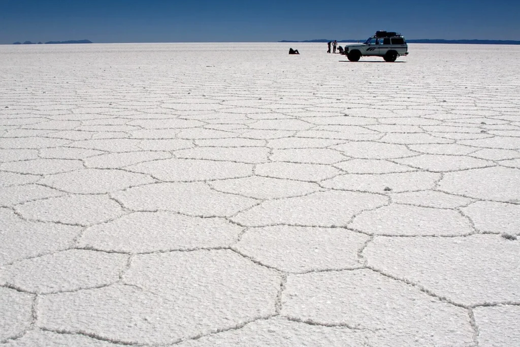 The dry-season surface of the Salar de Uyuni, patterned with pale hexagonal salt-crust ridges stretching to the horizon.