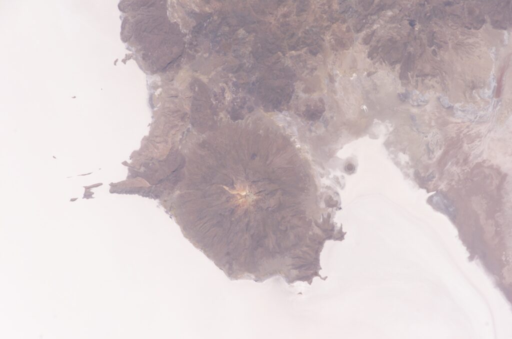 Astronaut photograph from the International Space Station showing the white expanse of the Salar de Uyuni beside the dark dormant volcano Mount Tunupa.