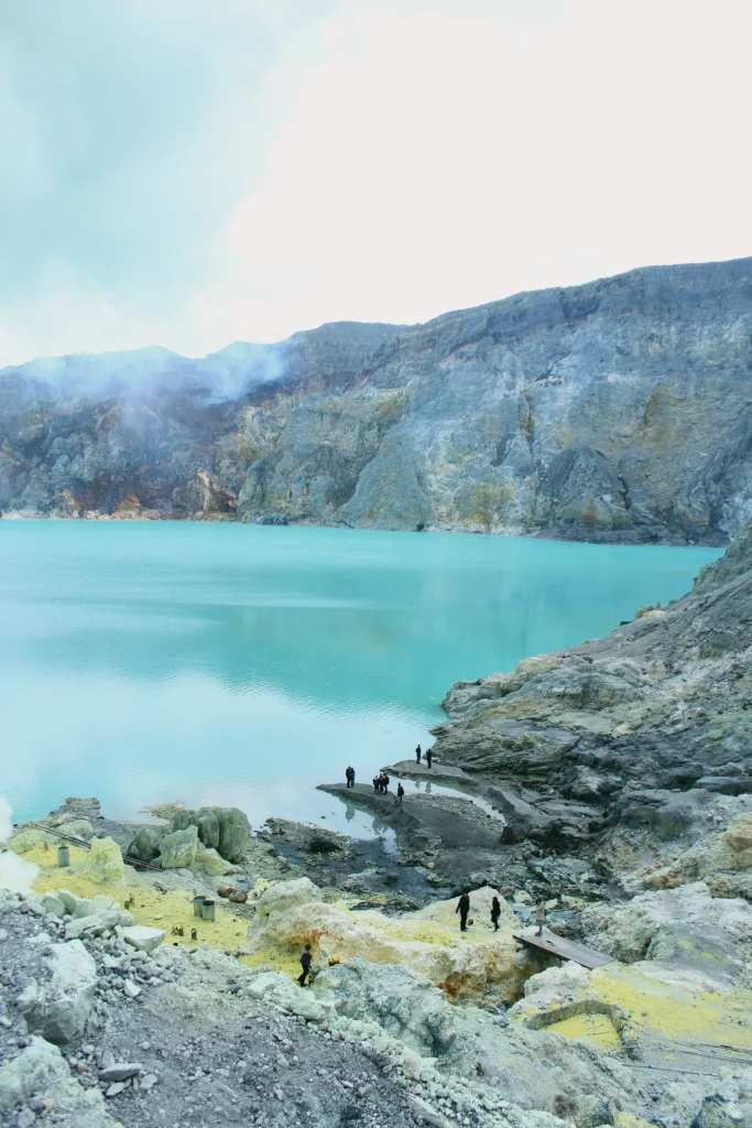 Turquoise hyperacidic crater lake of Kawah Ijen surrounded by steaming yellow sulfur cliffs