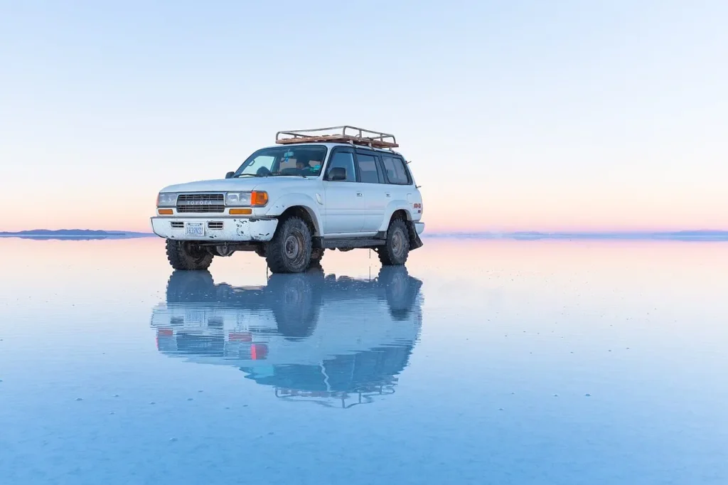 A vehicle and sky perfectly mirrored on a thin film of water covering the Salar de Uyuni salt flat, so that the horizon dissolves into reflected cloud.