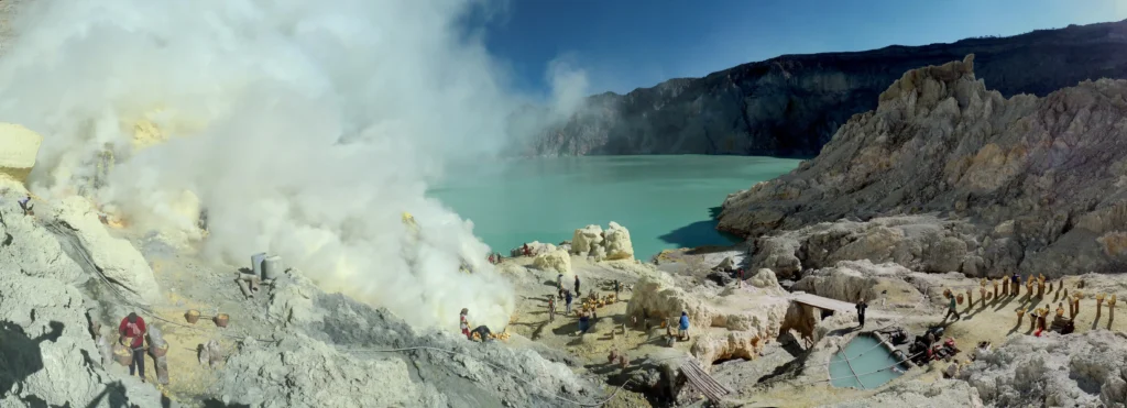 Panorama of the Kawah Ijen sulfur works with ceramic pipes, yellow sulfur deposits, and the acid lake