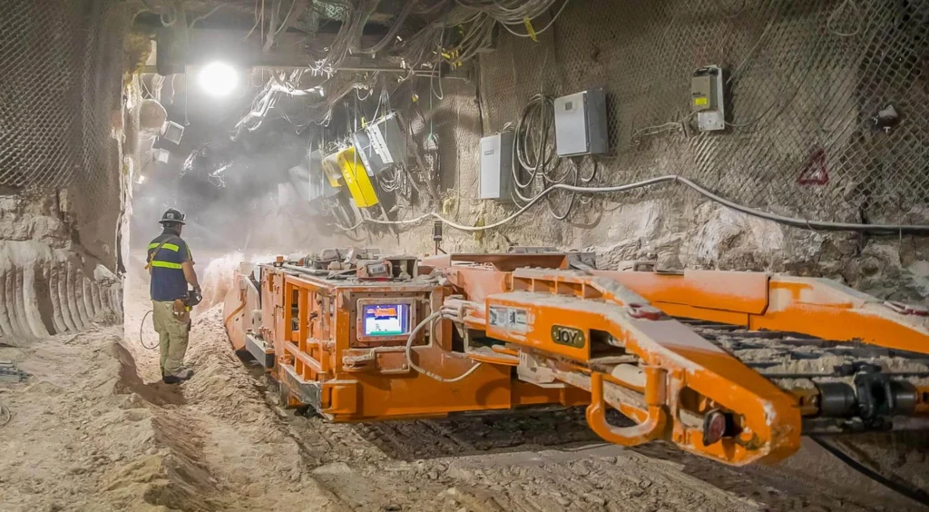 A worker stands beside large mining equipment in an underground salt repository at the Waste Isolation Pilot Plant, illustrating deep geological disposal of nuclear waste.