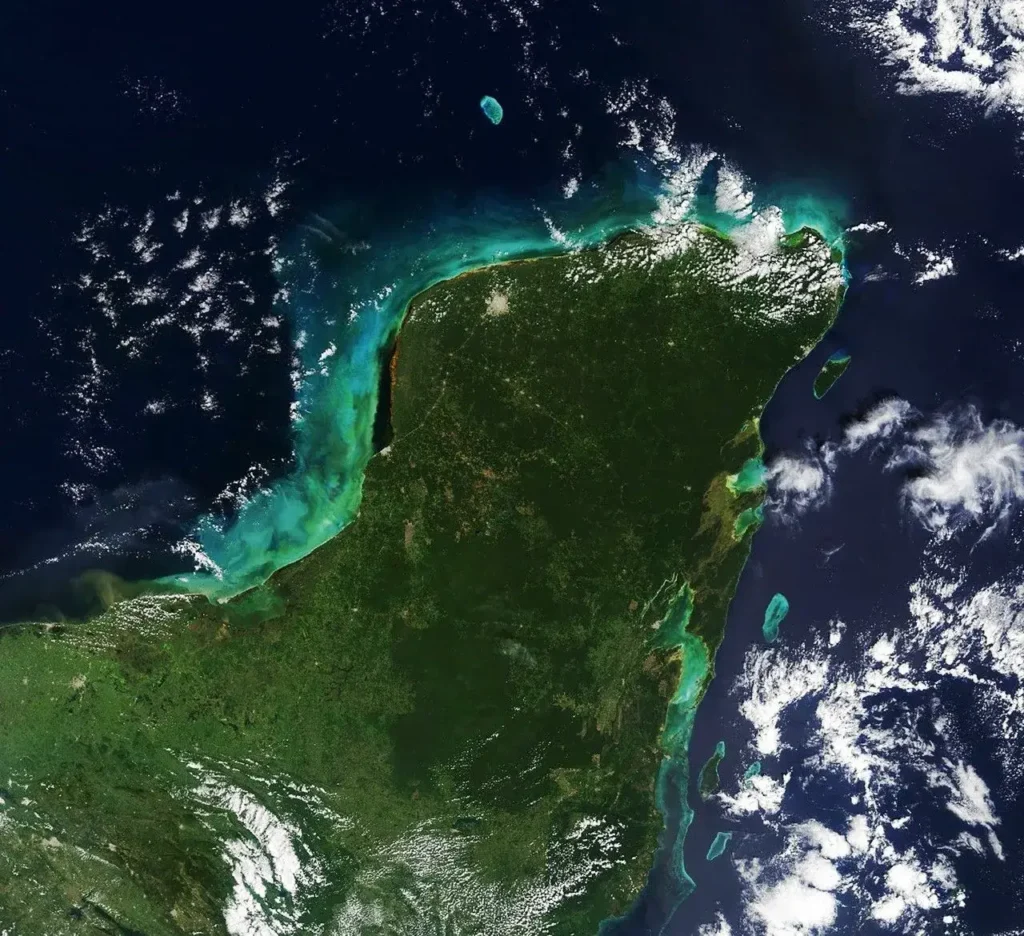 Satellite view of the Yucatán Peninsula and surrounding turquoise Caribbean waters, the limestone platform riddled with karst features that produce cenotes and blue holes