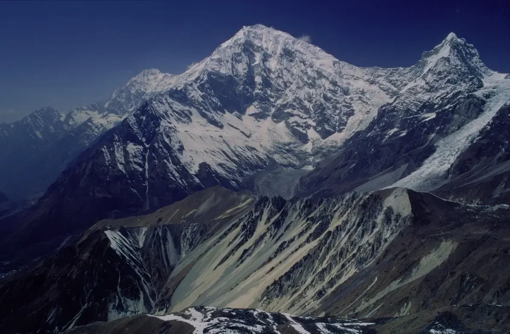 Snow-covered Langtang Lirung rising above debris-covered valley glaciers under a blue sky.