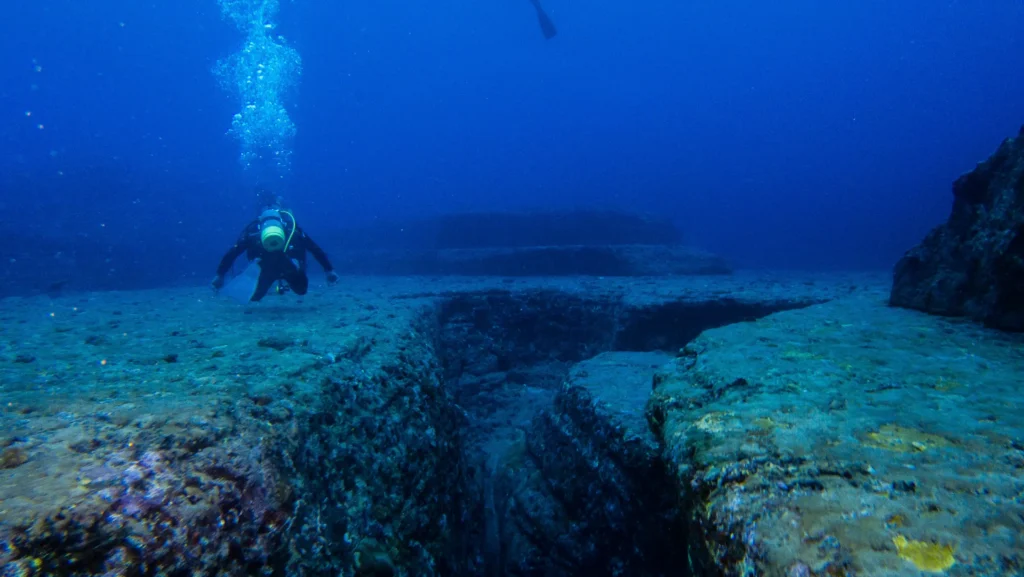 Scuba divers swimming beside the terraced sandstone steps of the Yonaguni underwater pyramid formation