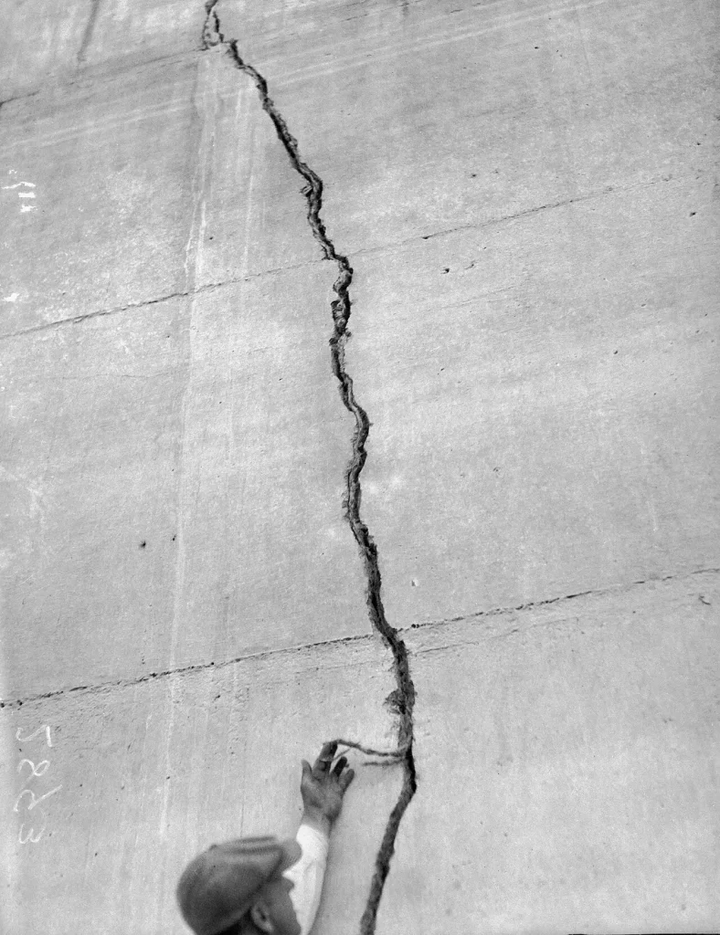 A man in a hat and overcoat pointing at a large crack in the surviving concrete of the dam