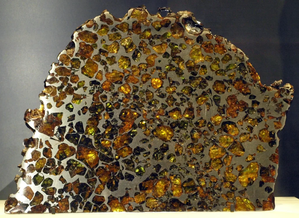 A backlit slice of the Esquel pallasite meteorite showing green olivine crystals in iron-nickel metal