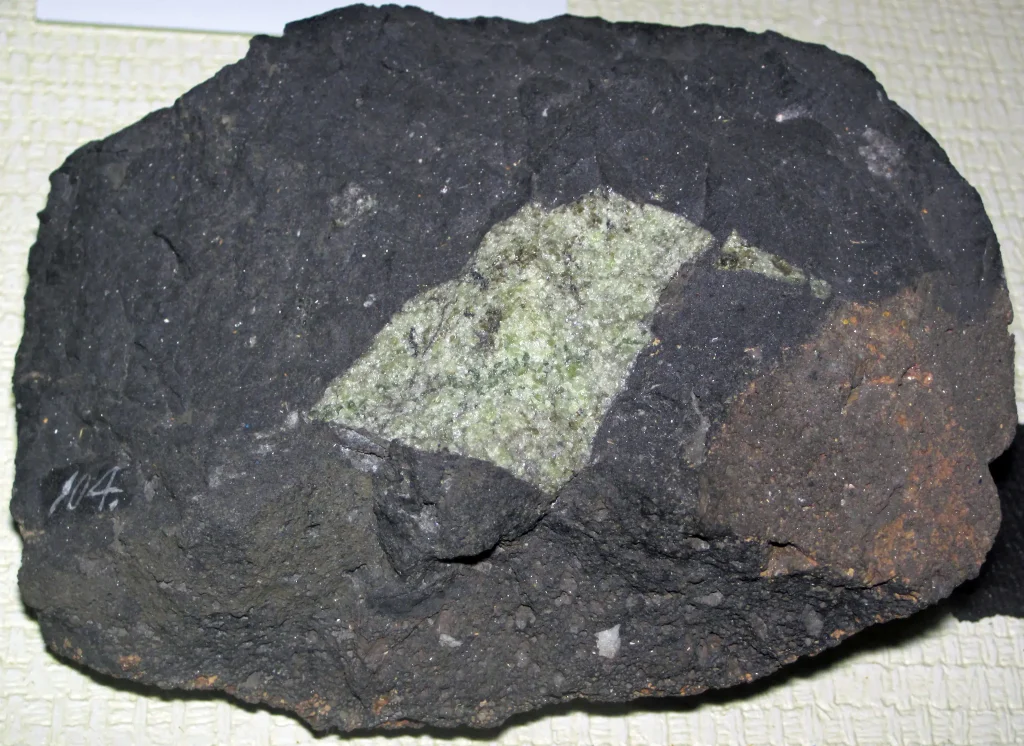 A green peridotite mantle xenolith embedded in dark basalt, a piece of Earth's mantle carried to the surface by a volcano