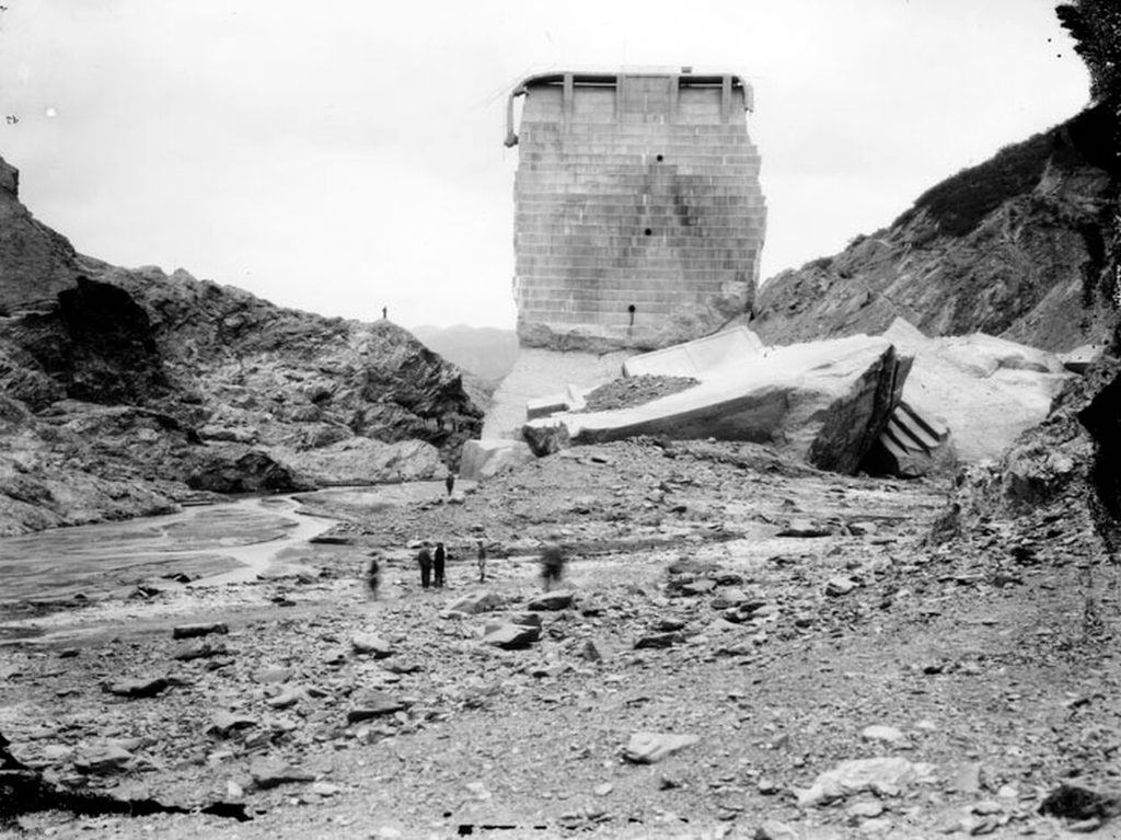 The surviving center monolith of the dam with huge broken concrete blocks heaped at its foot